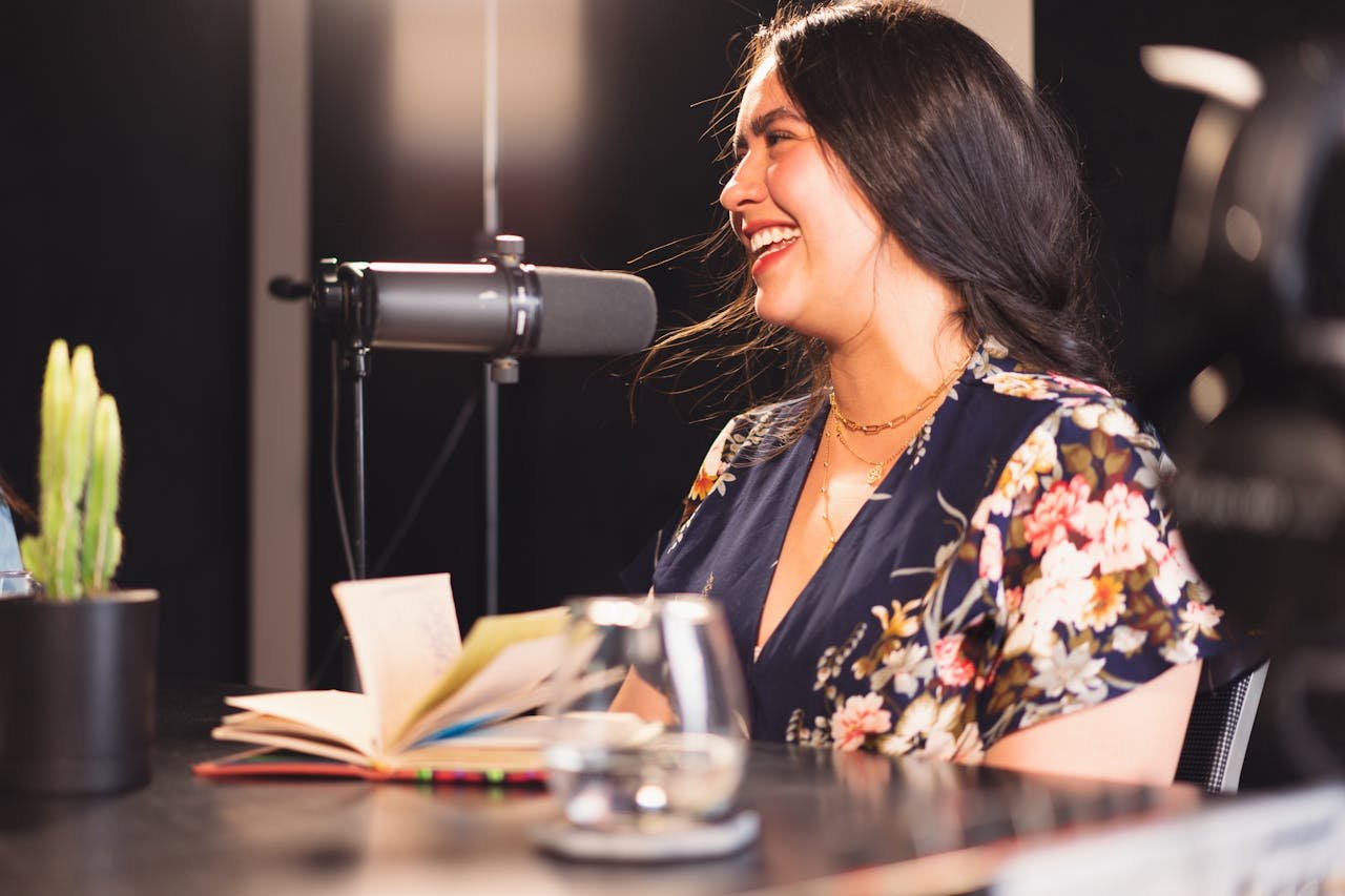 Woman in a vibrant studio setting recording a podcast with enthusiasm and expression.